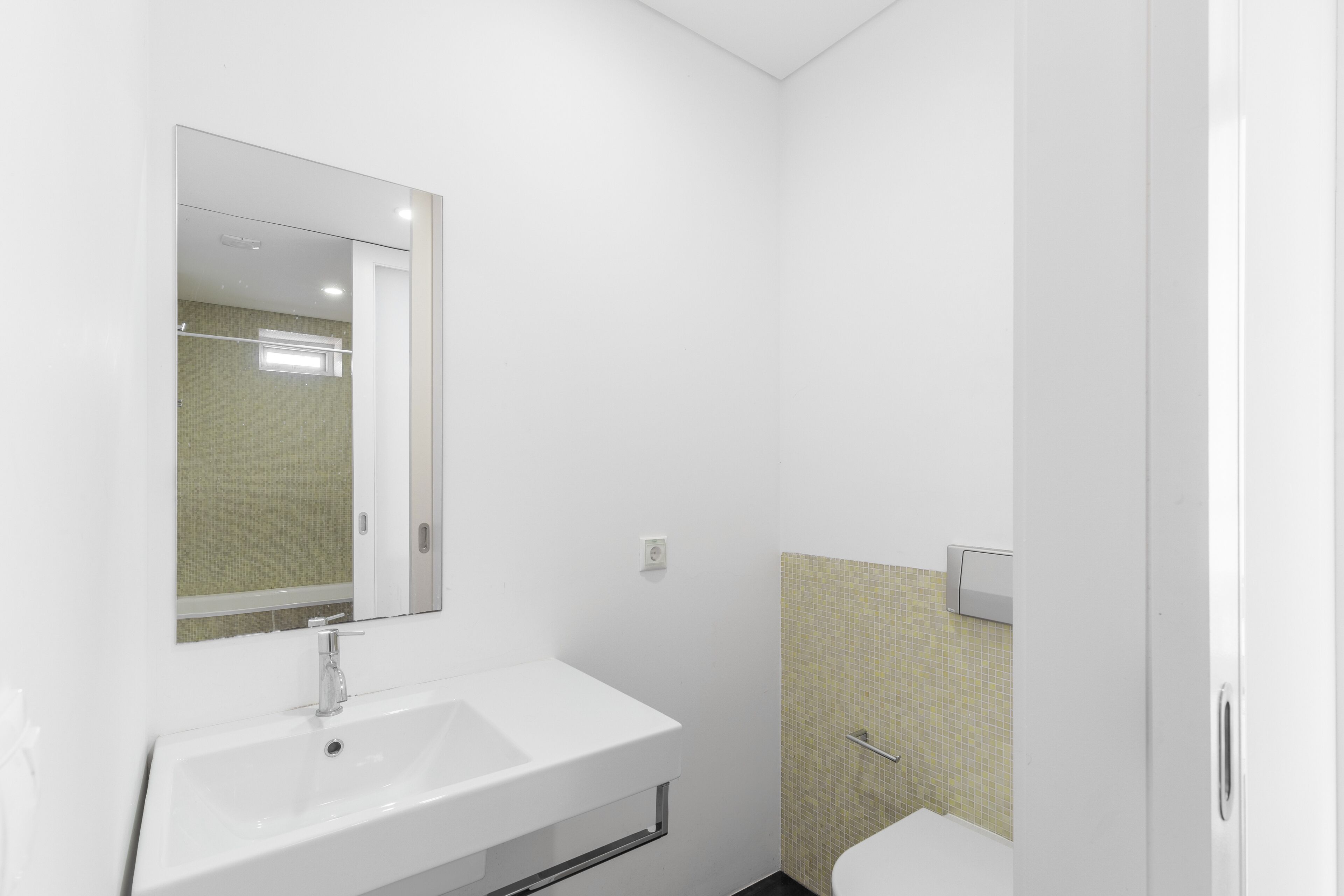 Un baño moderno con lavamanos, espejo e inodoro blancos.