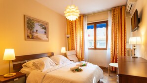 A hotel room with a bed, bedside tables, a desk, a chair, a window with curtains, and a painting on the wall. - LE FRANCE-MASSENET AP3015 by RIVIERA HOLIDAY HOMES (Niza)