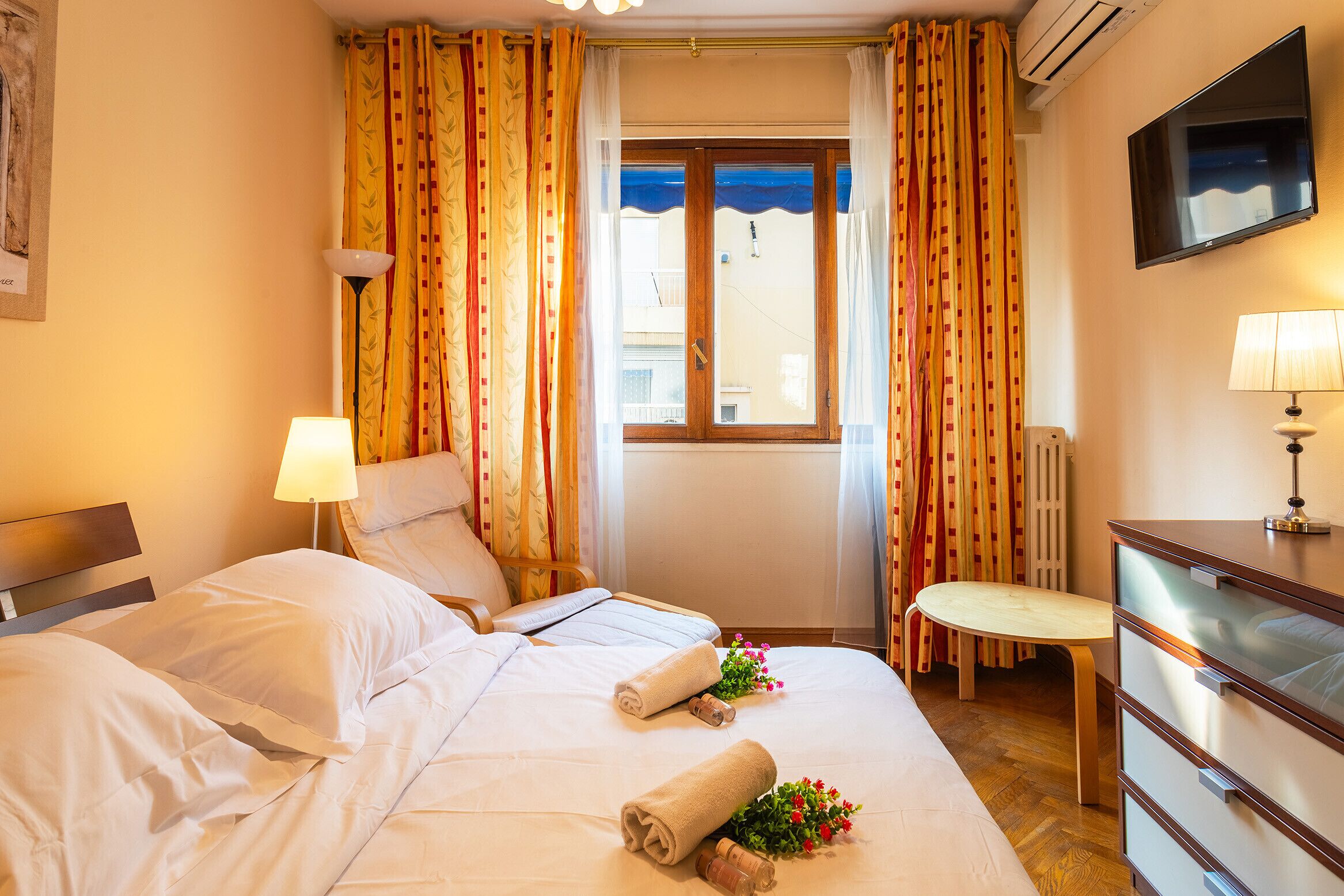 A hotel room with a bed, a desk, a chair, a TV, and a window with curtains.