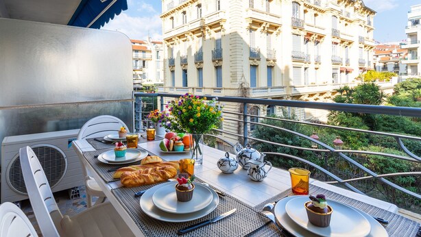 A balcony with a table set for breakfast, including croissants and pastries, and a view of a historic building in the background. - LE FRANCE-MASSENET AP3015 by RIVIERA HOLIDAY HOMES (Niza)