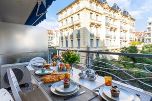 Un balcon avec une table dressée pour le petit-déjeuner, comprenant des croissants et des viennoiseries, et une vue sur un bâtiment historique en arrière-plan.
