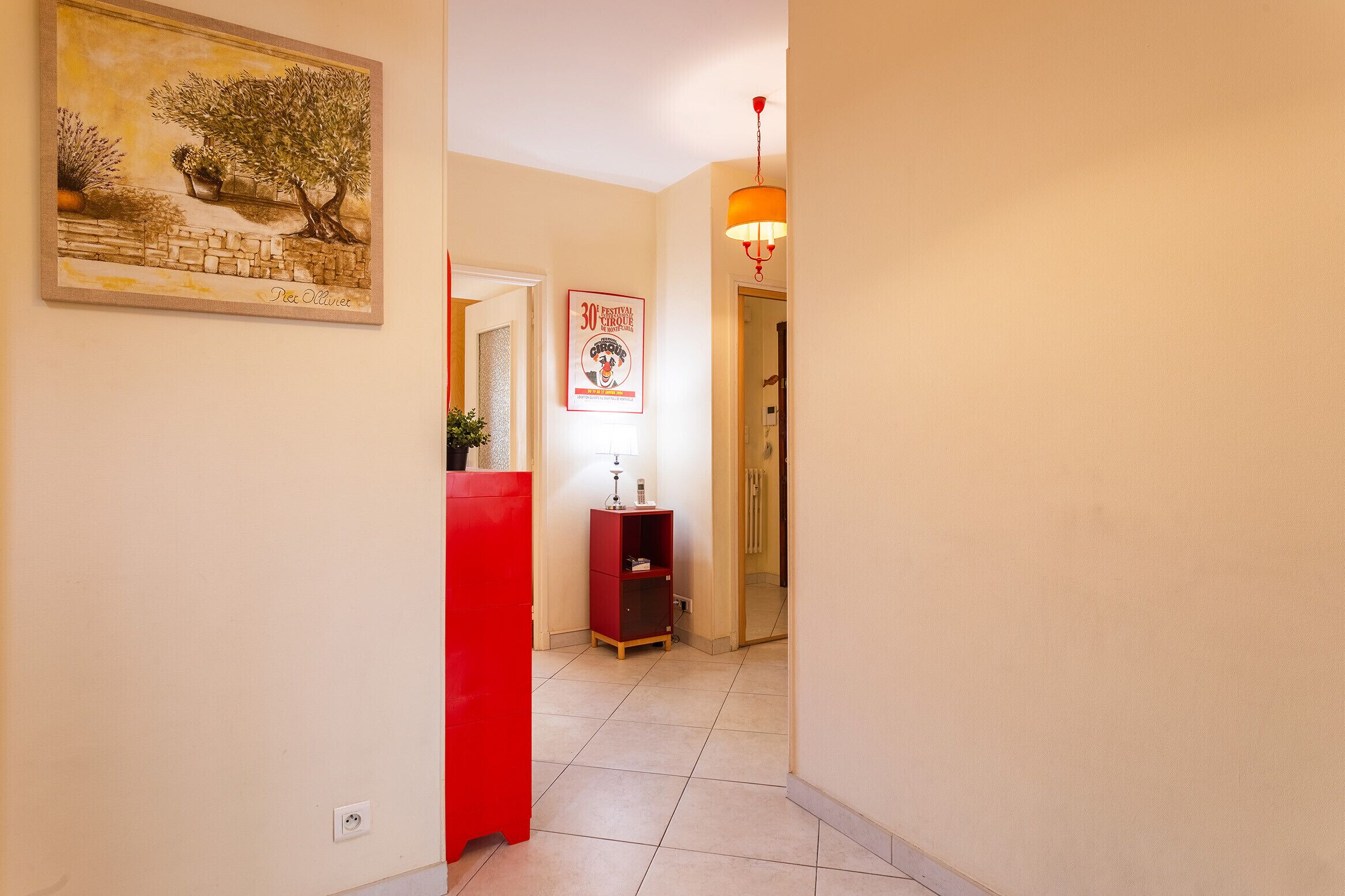 A hallway with a red cabinet, a framed painting, a red lamp, and a door leading to another room.