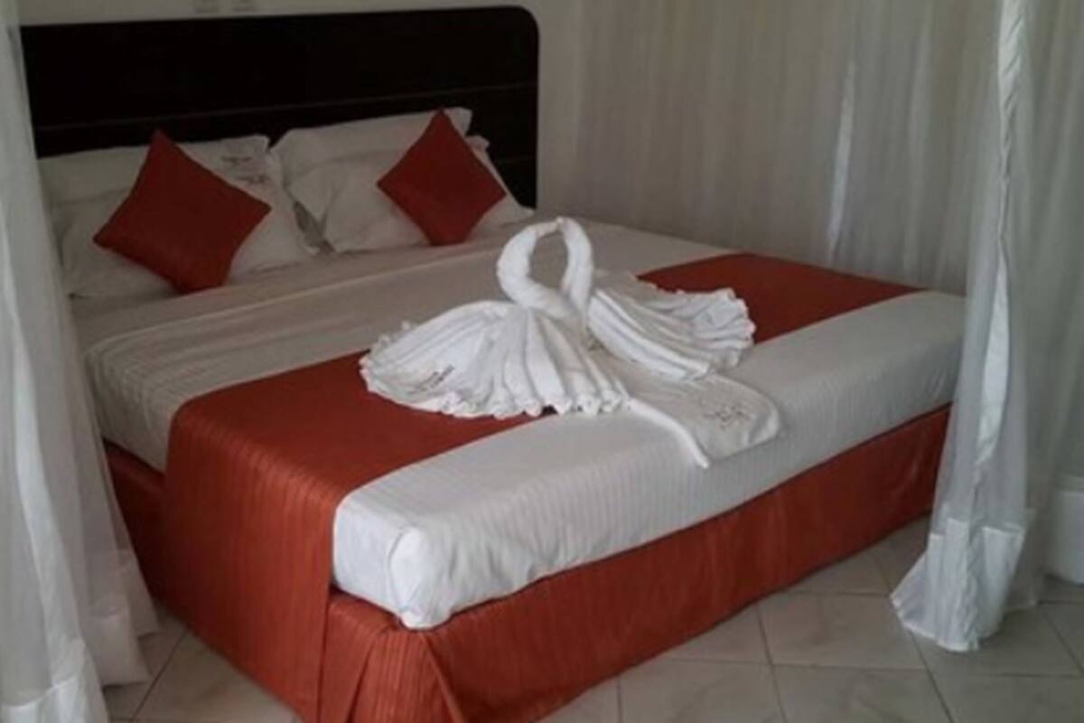 A neatly made bed with a red bedspread and white pillows, a white headboard, and a white canopy.