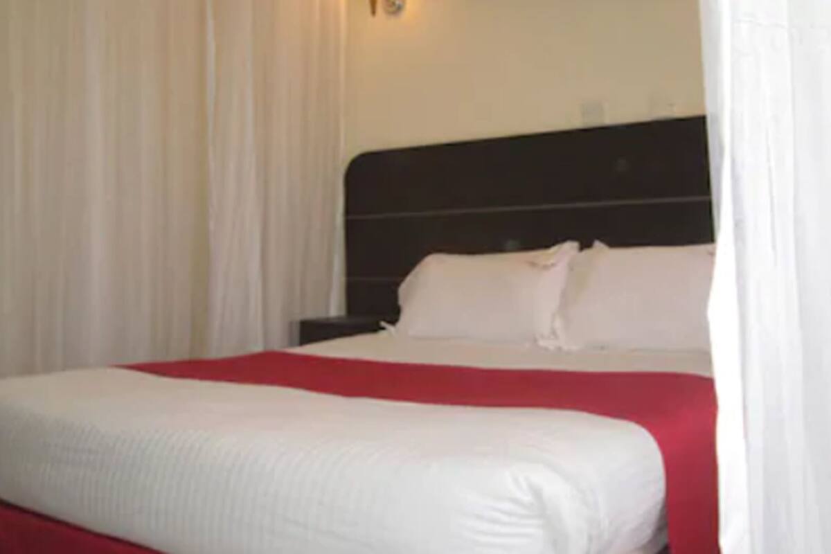 A hotel room with a bed, white curtains, and a black headboard.