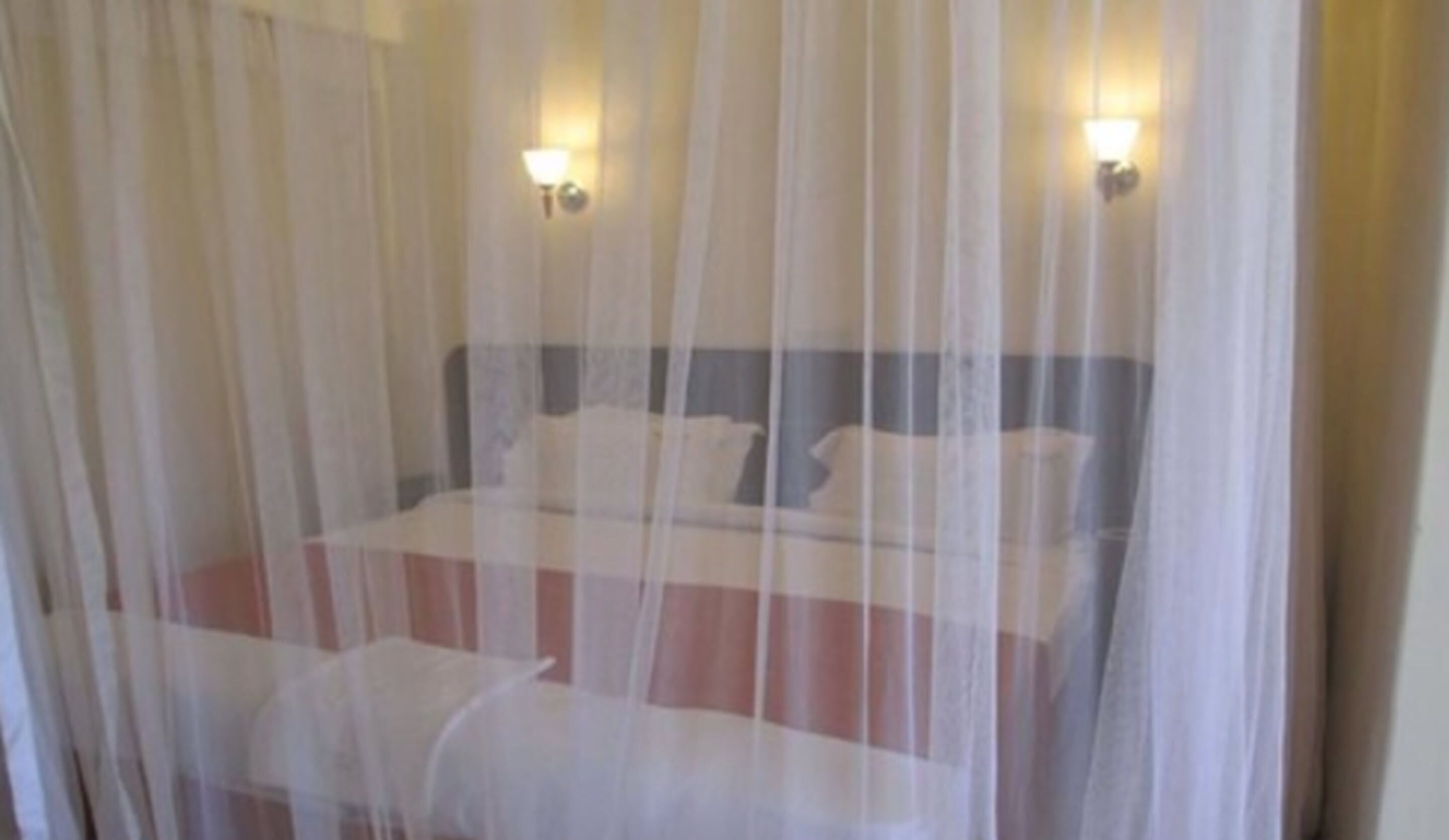 A bed with a striped bedspread and white pillows, covered by a sheer white curtain.