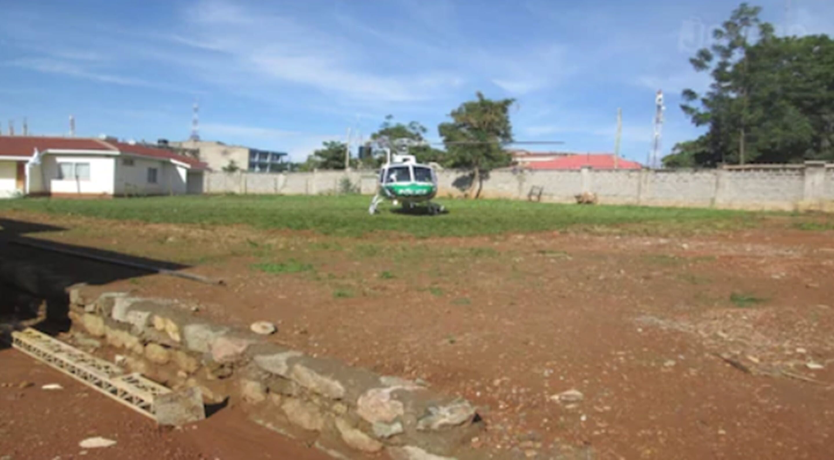 A helicopter on a dirt field with a stone wall in the foreground.