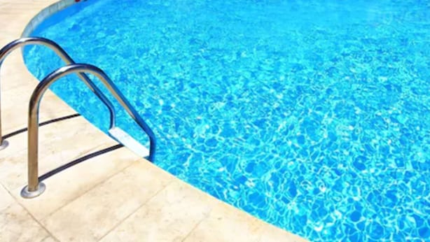 Une piscine avec une eau d’un bleu limpide et une échelle métallique sur le côté gauche.