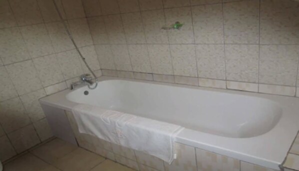 Un baño con bañera, paredes de azulejos y ducha.