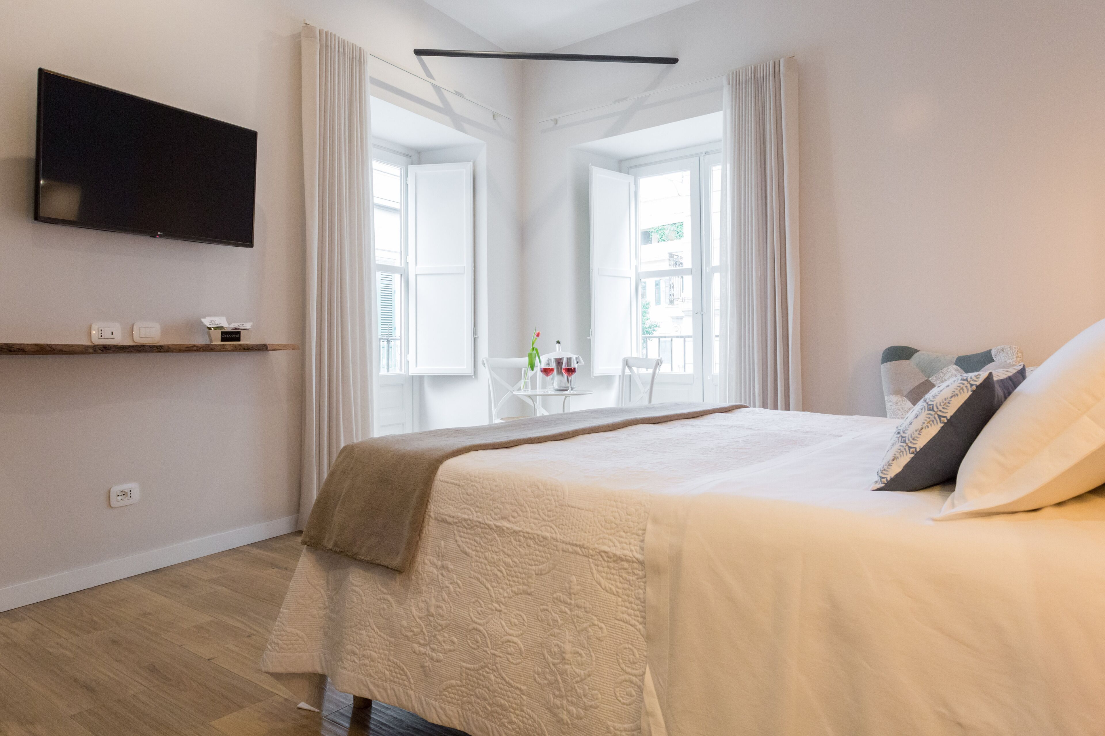 Un dormitorio moderno con una cama grande, un televisor montado y un ventanal con cortinas.