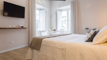 Un dormitorio moderno con una cama grande, un televisor montado y un ventanal con cortinas.