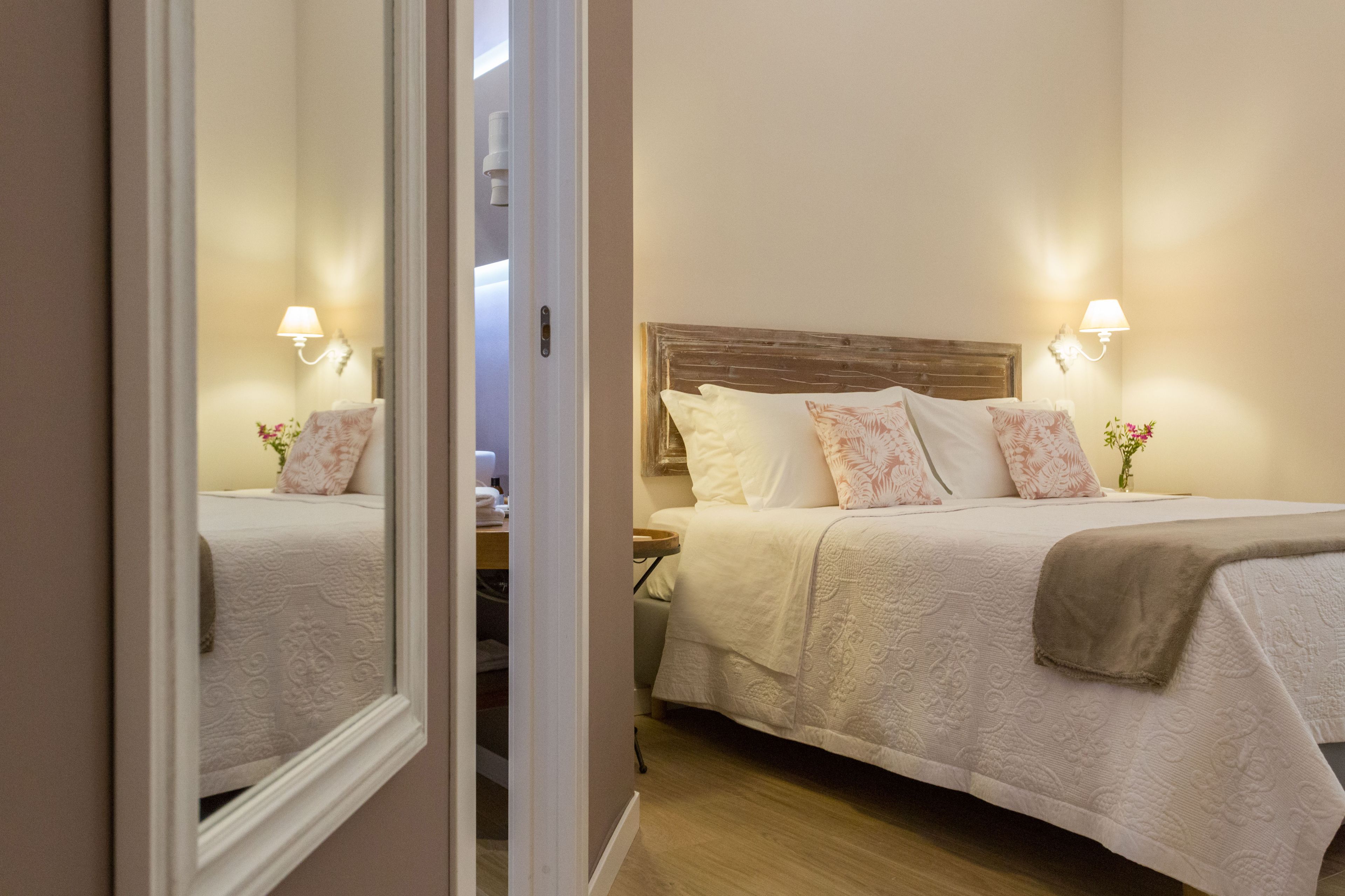A neatly made bed with a wooden headboard, two bedside lamps, and a mirror reflecting the room.