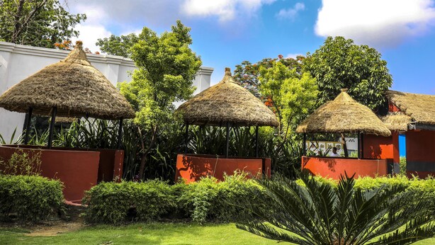 Thatched-roof structures with red walls, surrounded by lush greenery and trees. - Siddhartha Cottage Butwal (Butwal)