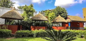 Thatched-roof structures with red walls, surrounded by lush greenery and trees. - Siddhartha Cottage Butwal (Butwal)
