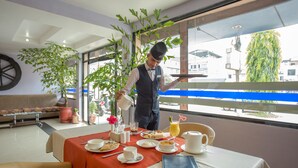 A breakfast setting with a waiter pouring a drink, a table with plates of food, a vase with flowers, and a view of the outside. - Siddhartha Cottage Butwal (Butwal)