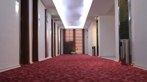 A hallway with a red carpet, wooden doors, and a plant in the center.