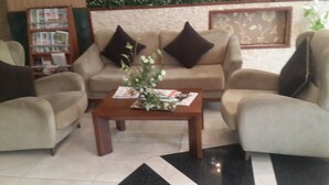 A living room with a beige sofa set, a wooden coffee table with magazines, and a patterned rug.