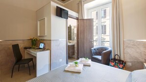 A hotel room with a bed, a desk with a computer, a chair, and a window with a view of buildings. - Suite Horti Sallustiani (Rome)