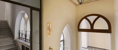 A staircase leading to a balcony with a checkered floor, a wall-mounted light fixture, and a decorative ceiling.