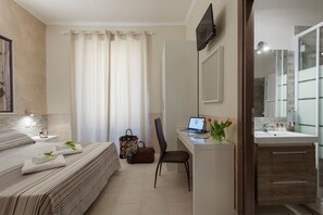 A hotel room with a bed, a desk with a laptop, a chair, a bathroom with a mirror, and a TV mounted on the wall. - Suite Horti Sallustiani (Rome)