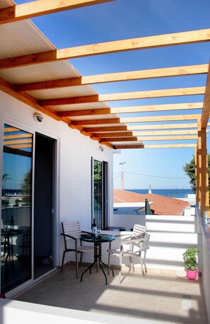 Varanda com vigas de madeira, porta de vidro, duas cadeiras, uma mesa e um vaso com planta.