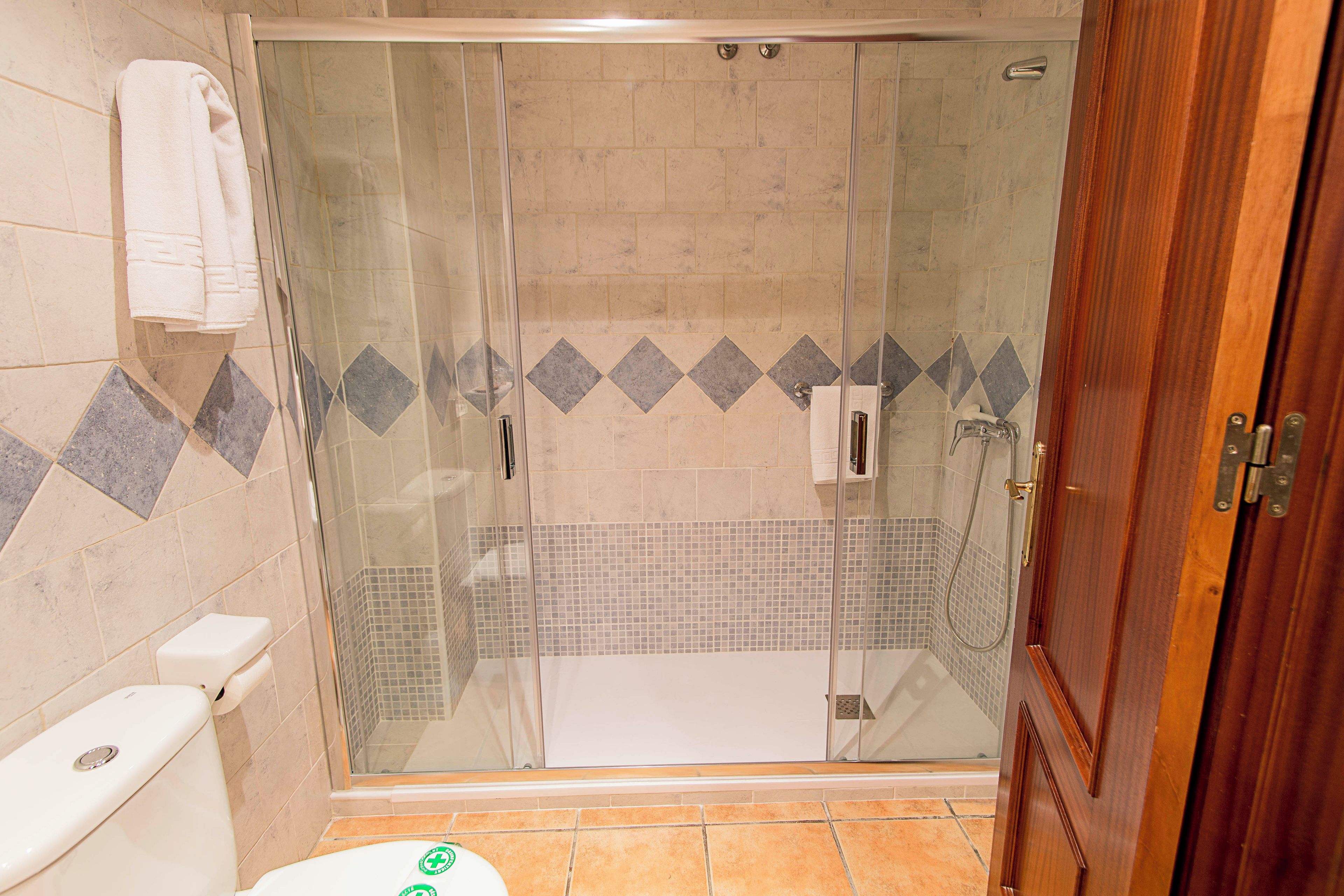 A glass-enclosed shower with a tiled floor and a wooden door.