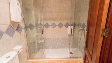 A glass-enclosed shower with a tiled floor and a wooden door.