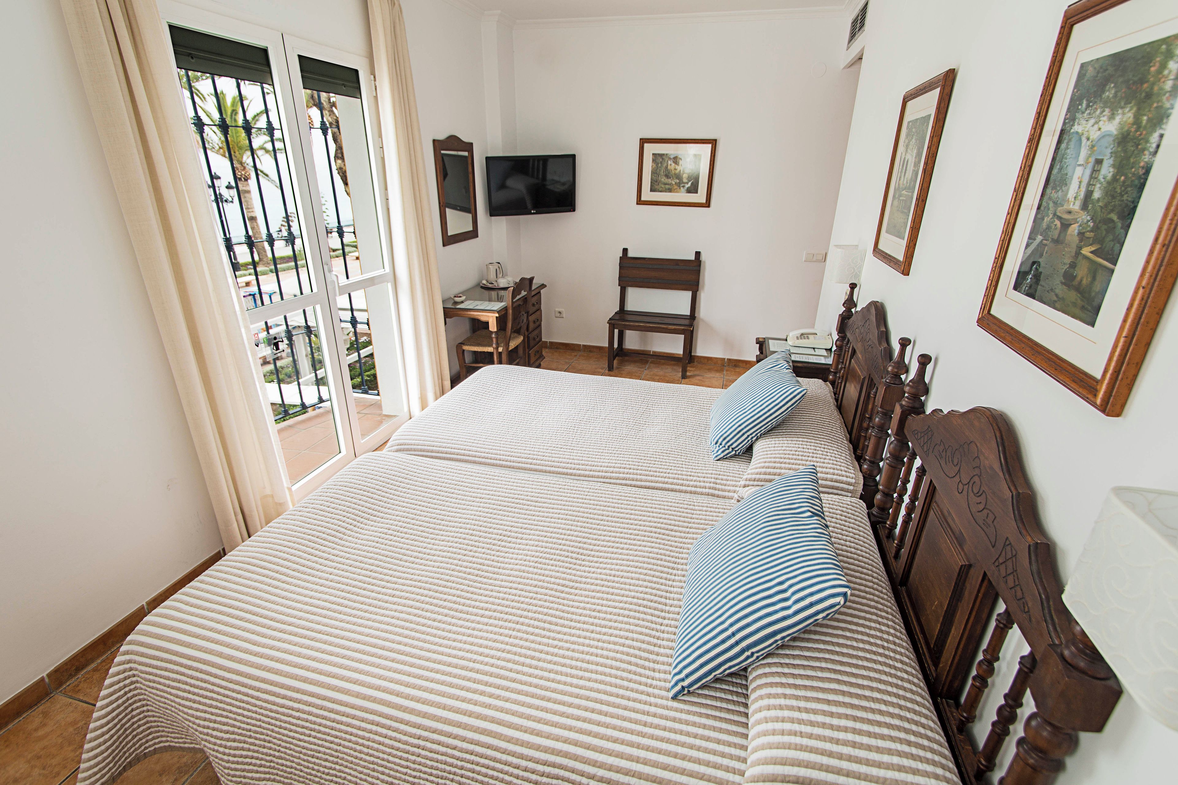 A bedroom with two beds, a desk, a chair, a television, and framed pictures on the wall.