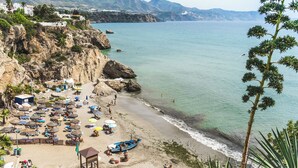 A beach with umbrellas, lounge chairs, and a lifeguard tower. - Marissal (Nerja)