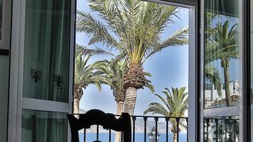 A room with a view of palm trees and the sea through a glass door.