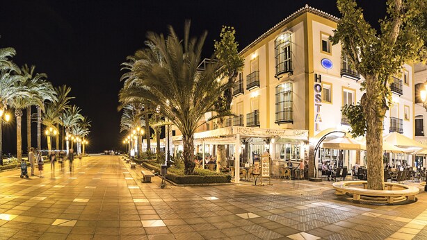 A well-lit square with a central fountain, surrounded by palm trees and buildings with balconies. - Marissal (Nerja)