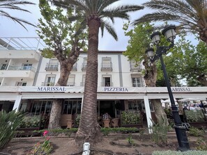 Een gebouw met de borden 'MARISSAL' en 'PIZZERIA', omringd door palmbomen en potplanten.