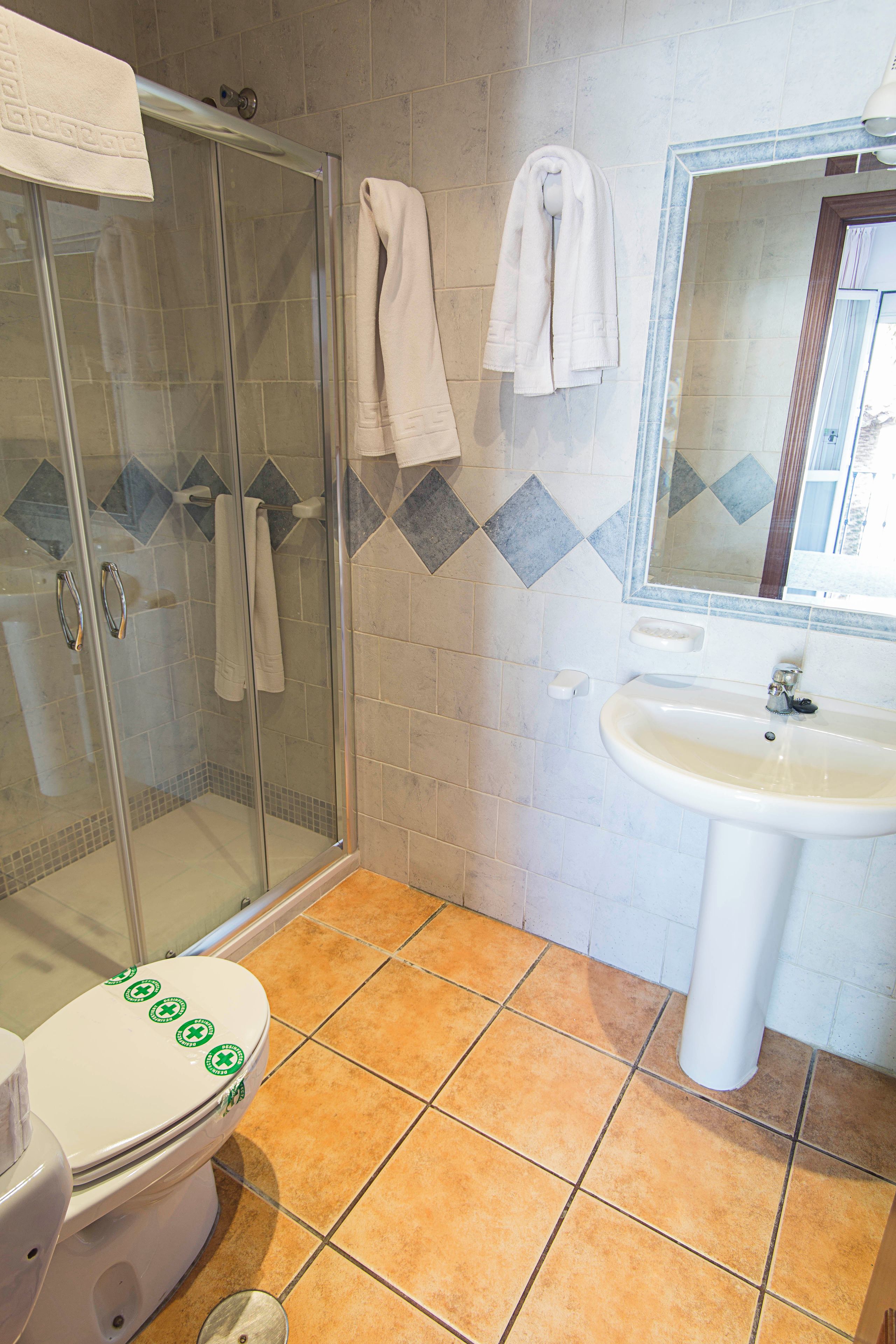 A bathroom with a glass shower enclosure, a white sink, and a toilet with green stickers.