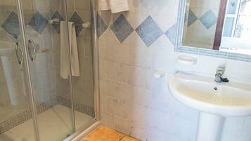 A bathroom with a glass shower enclosure, a white sink, and a toilet with green stickers.