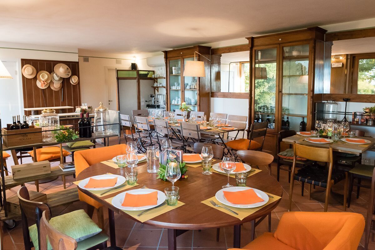 Un espace repas avec plusieurs tables dressées pour un repas, entouré de chaises et avec un coin cuisine en arrière-plan.