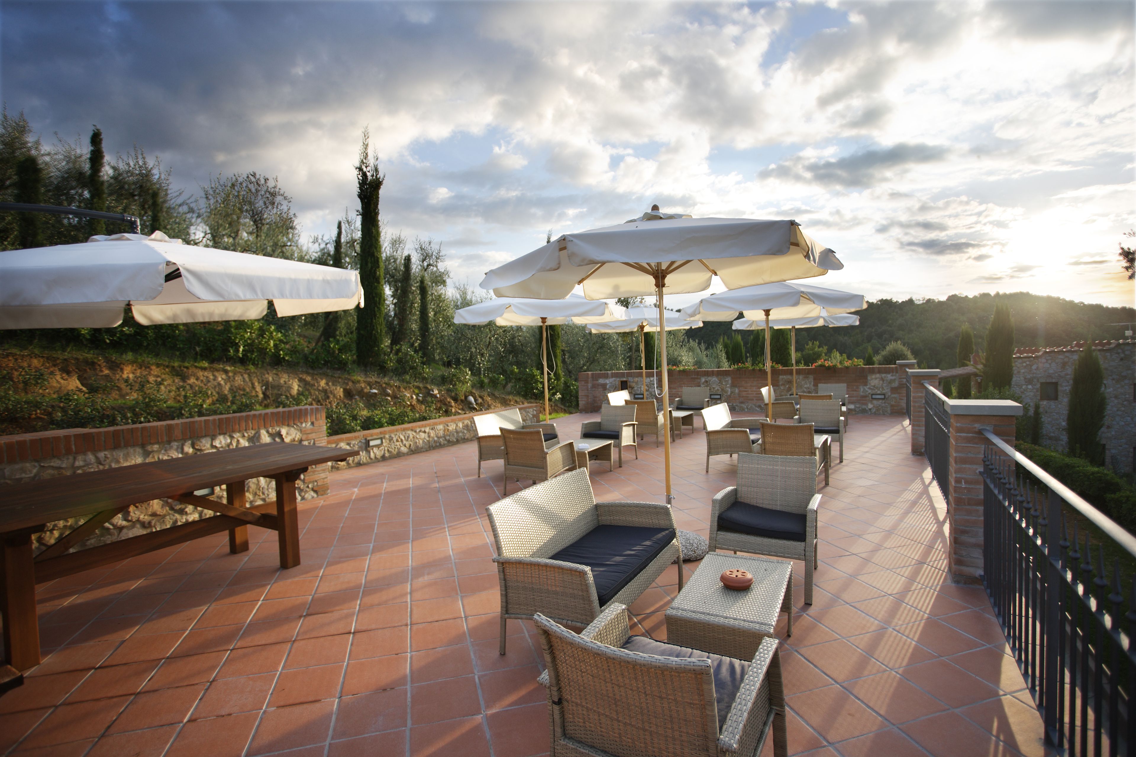 Eine Terrasse im Freien mit Korbmöbeln, weißen Sonnenschirmen und einer Steinmauer.