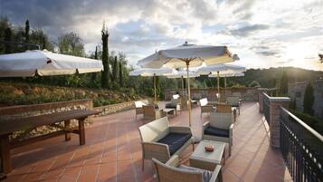 Eine Terrasse im Freien mit Korbmöbeln, weißen Sonnenschirmen und einer Steinmauer.