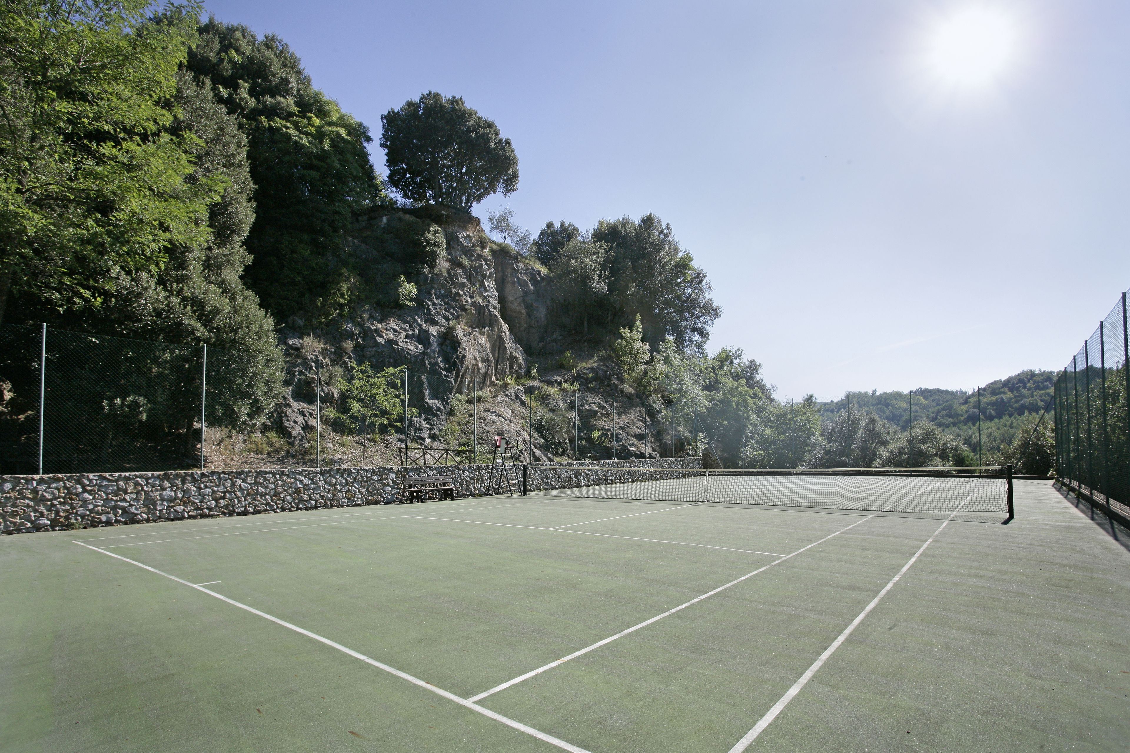 An outdoor tennis court with a stone wall and trees in the background.