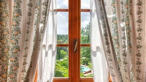 A window with floral curtains, a wooden frame, and a view of a green landscape. - Il Torrino Country Resort (Montaione)