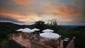 An outdoor patio with multiple white umbrellas, a brick wall, and a wooden table. - Il Torrino Country Resort (Montaione)