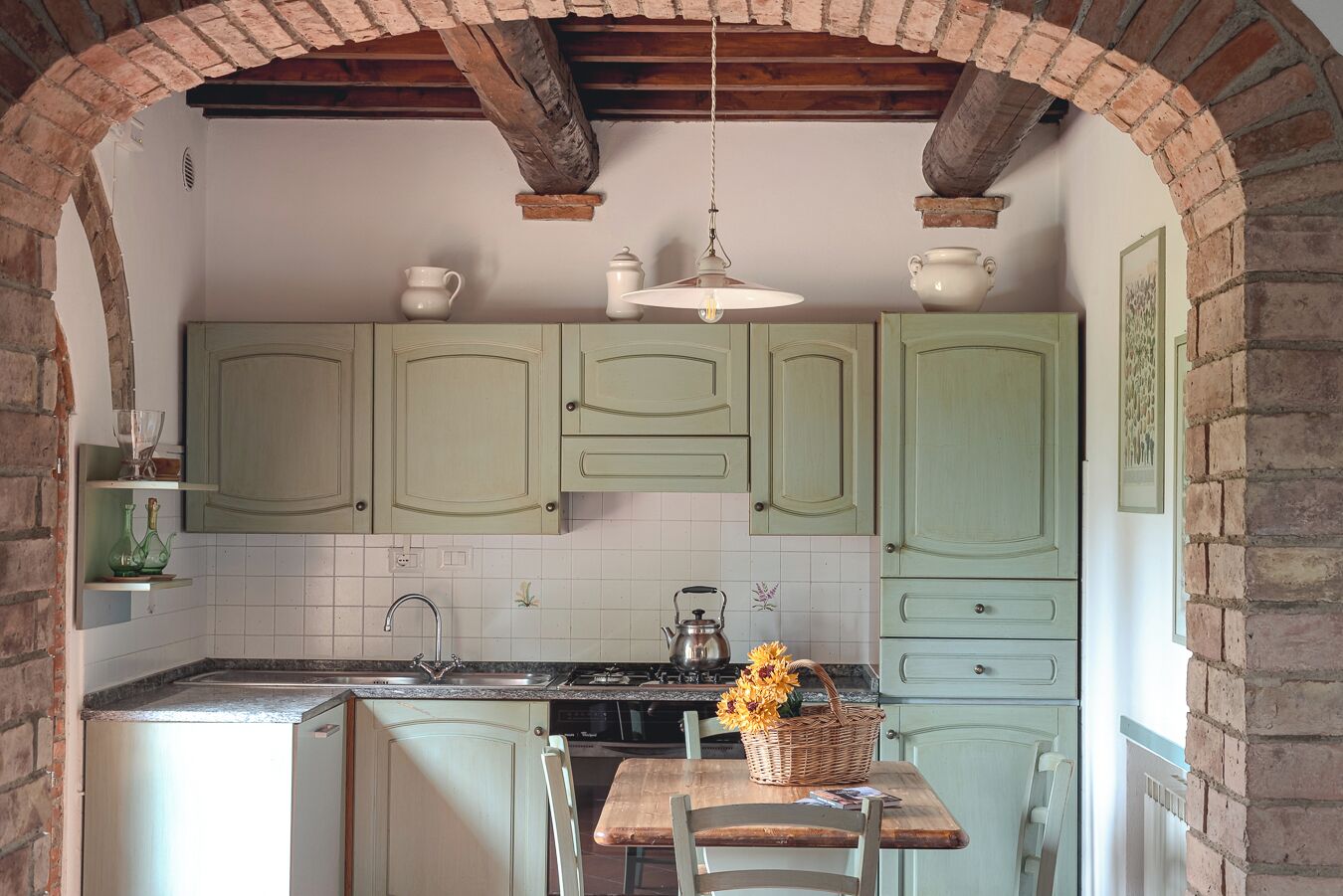 Una cocina con armarios verdes, una mesa de madera y una lámpara colgante.