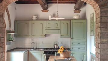 Una cocina con armarios verdes, una mesa de madera y una lámpara colgante.