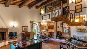 A spacious living area with a high ceiling, wooden beams, a staircase, and a dining area. - Il Torrino Country Resort (Montaione)