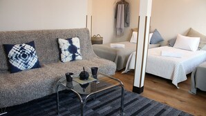 A modern hotel room with a grey sofa, a small glass table with two cups, a bed with striped bedding, and a wooden floor. - Lodge Romulus (Rusutsu)