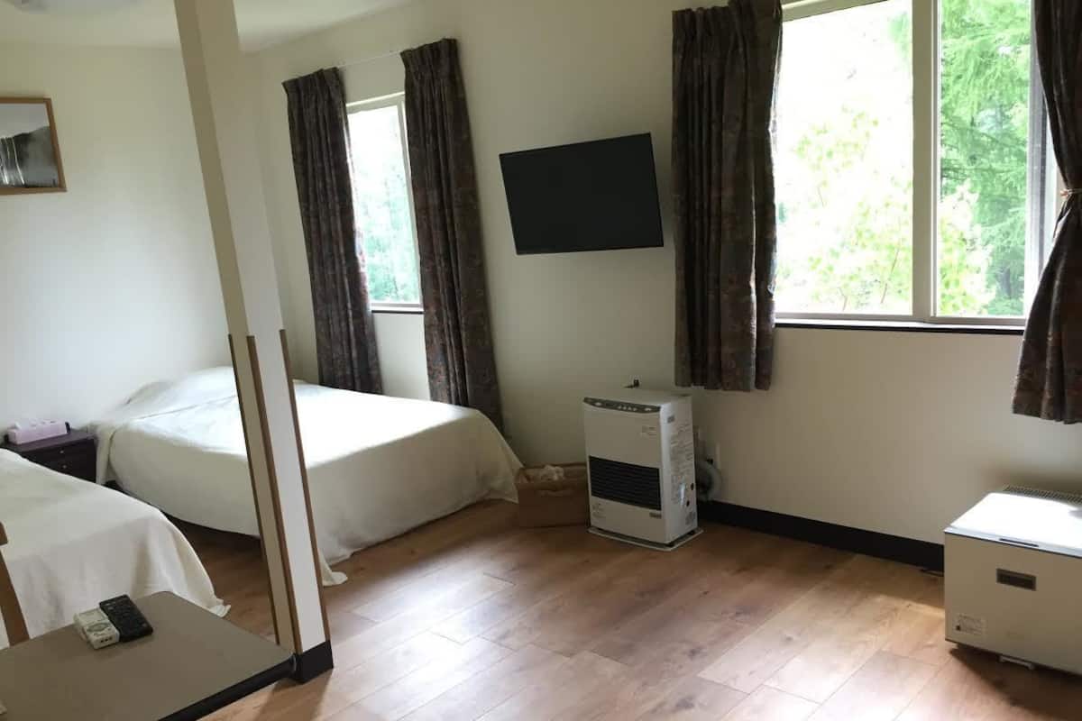 Quarto de hotel com duas camas, televisão, aquecedor e janela com cortinas.