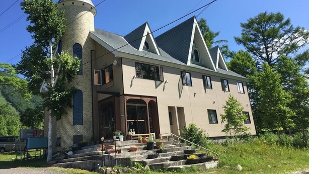 A two-story building with a tower, a front entrance with steps, and a small porch area. - Lodge Romulus (Rusutsu)