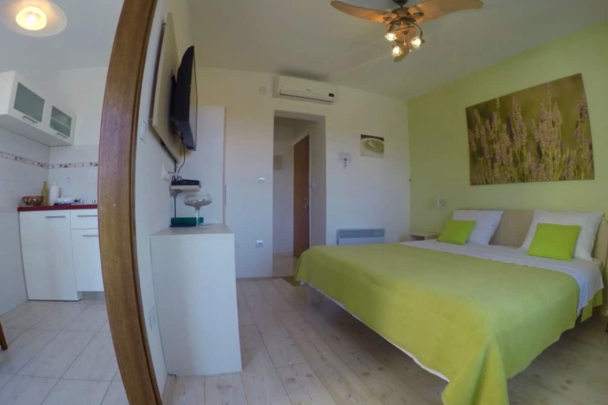 A bedroom with a bed, a desk, a television, and a painting on the wall.