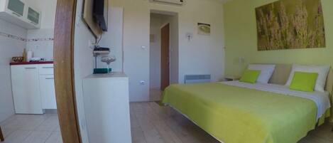 A bedroom with a bed, a desk, a television, and a painting on the wall.
