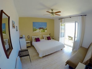 Un dormitorio con cama, ventilador de techo, mesita de noche, silla y ventana.