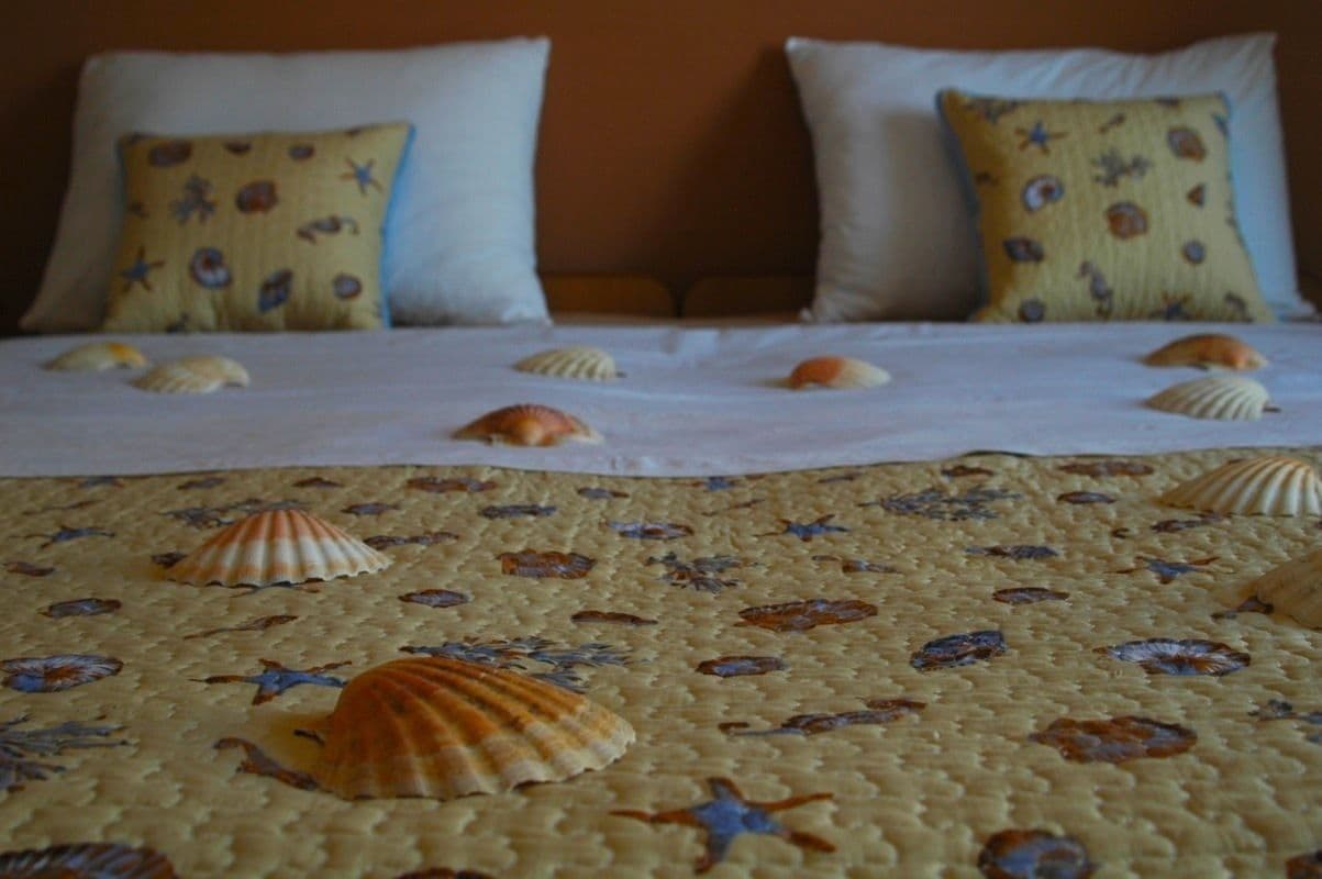 Een bed met een beddegoed met een getextureerde print van schelpen en zeesterren, omlijst door kussens met een maritiem patroon.
