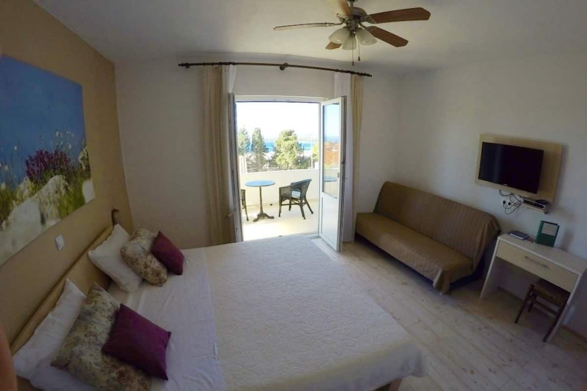 A hotel room with a bed, a desk, a television, and a balcony with a view.
